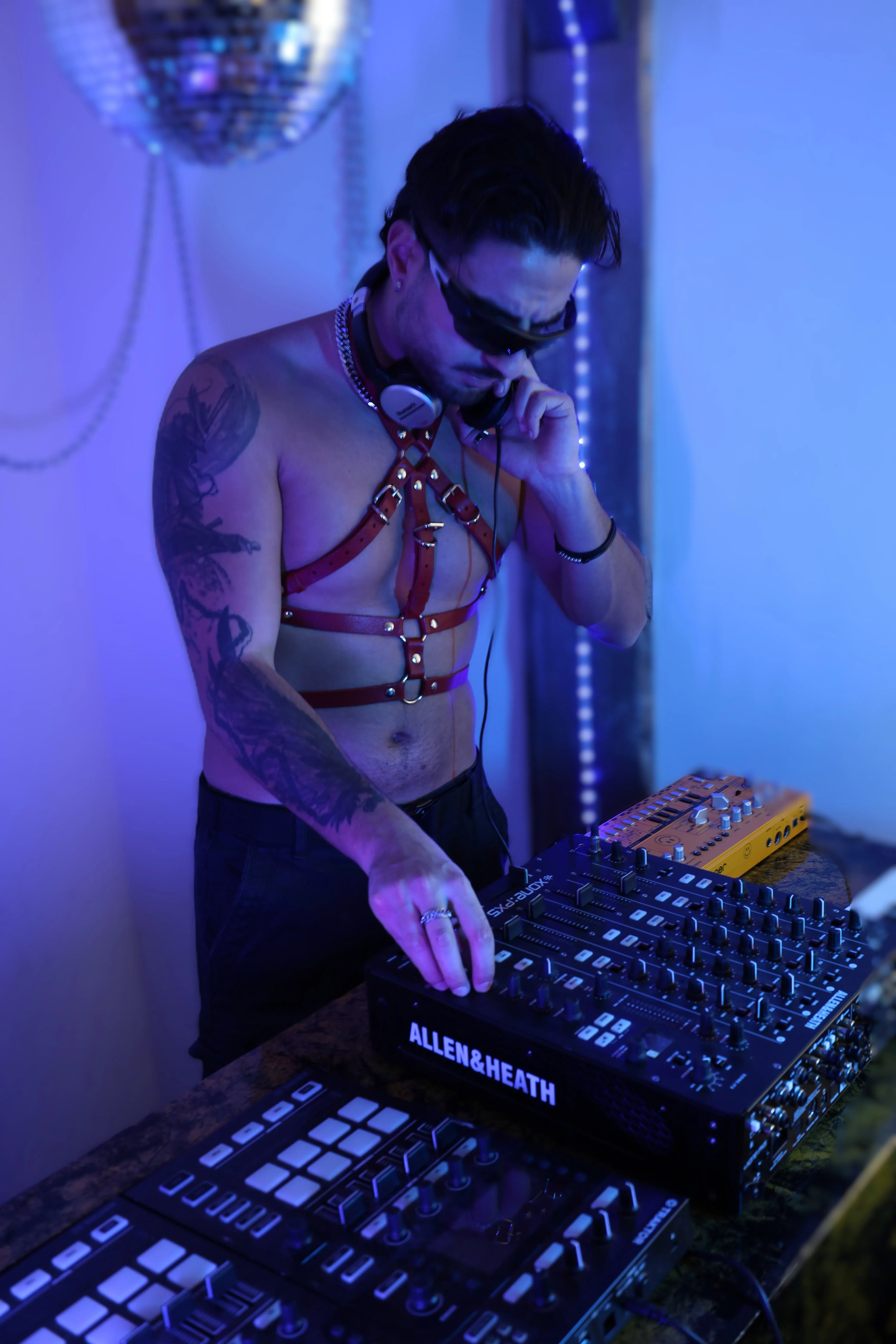 Mann als DJ trägt rotes Leder kinky Harness für Herren bei einer Techno-Performance am Mischpult